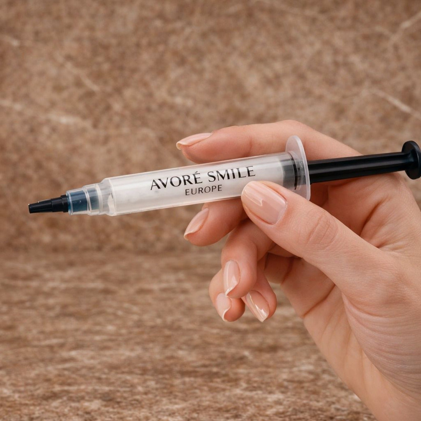 Avoré Smile Europe 12% PAP non-peroxide teeth whitening gel syringe, 3ml dental whitening treatment held in hand with a red marble backdrop 